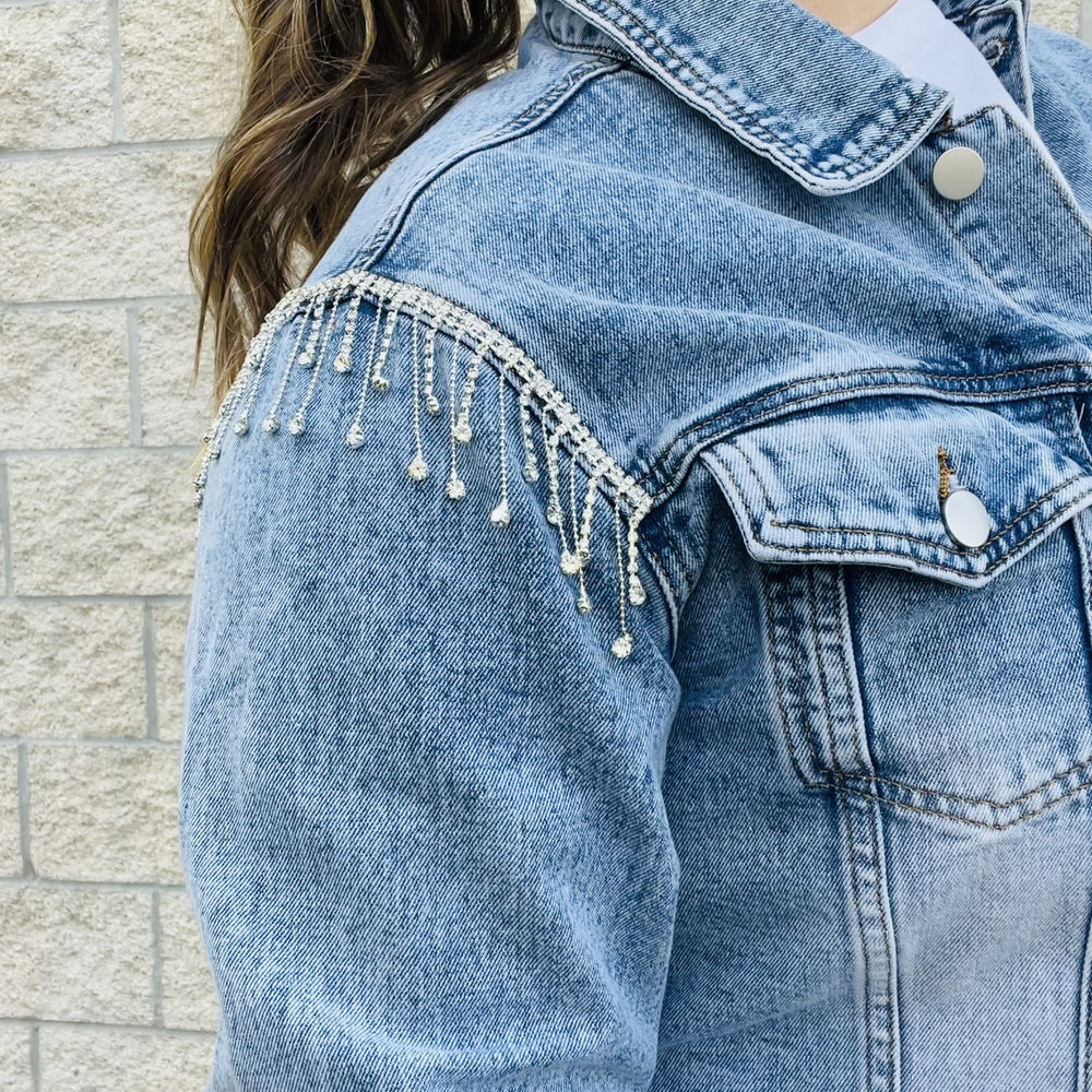 
                  
                    Elevate your style with this edgy denim jacket. With rhinestone details on the sleeves, this jacket will turn heads wherever you go. The distressed hemline gives it a unique edge that you'll love. Perfect for a night out or for everyday wear, this jacket is a must-have in your wardrobe.  Details Rhinestones details on sleeves Cropped Distress hemline 87% Cotton | 8% Poly | 5% Viscose
                  
                